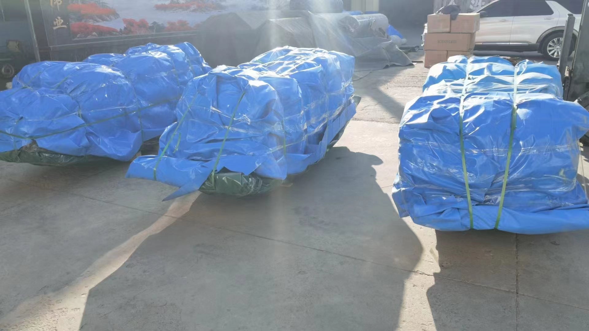 Several blue-tarped collapsible water tanks packaged on a concrete surface in an outdoor industrial area ready for shipping or storage.