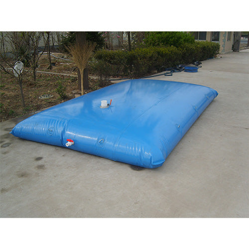 A large blue water storage bladder placed outdoors on a concrete surface, surrounded by greenery and a hose.