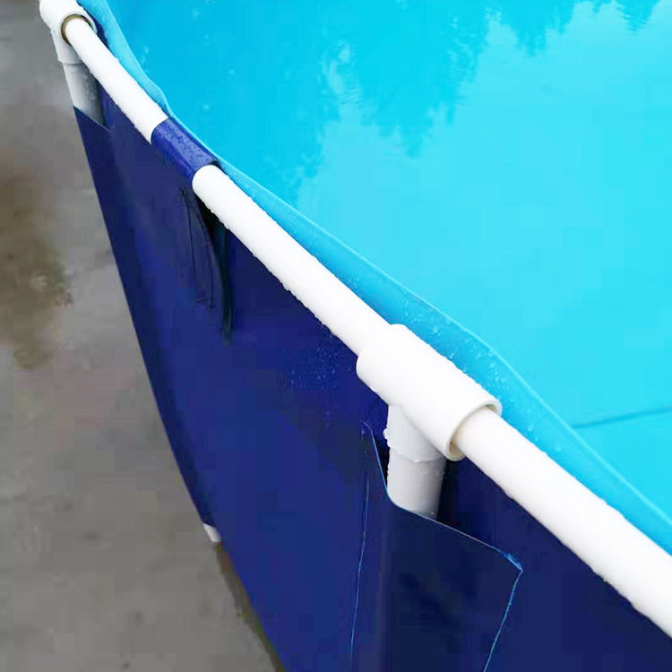 A blue above-ground pool filled with water, featuring a white frame with connecting pipes and a black fitting on the side, is set on a wet surface with greenery visible in the background.