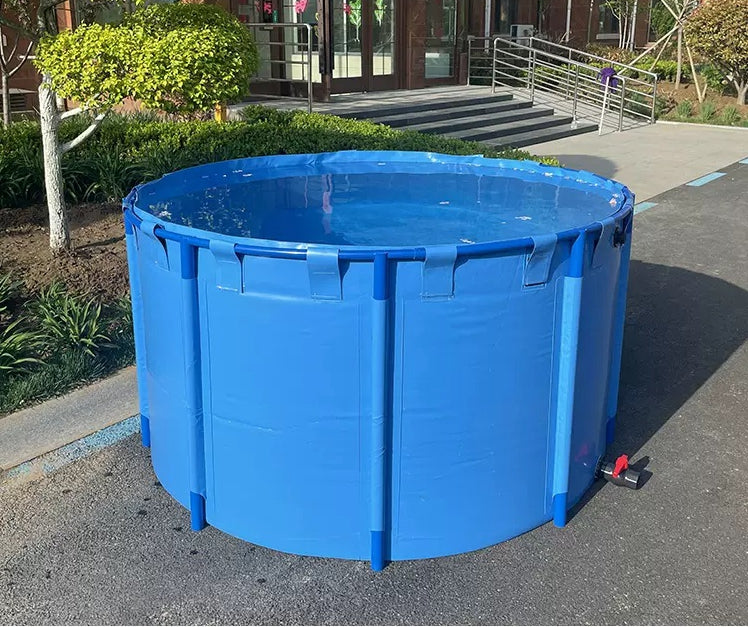 Blue collapsible fish water tank filled with water on a concrete surface outside a building, surrounded by greenery, perfect for portable water storage.