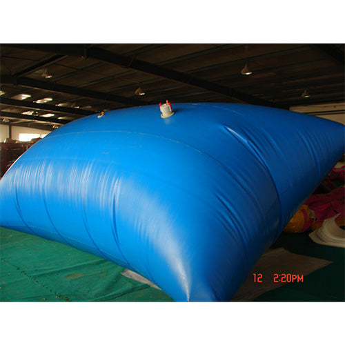 A large blue water storage bladder with a red and white valve placed on a green surface in a warehouse.