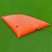 Large rectangular orange inflatable water storage bladder with multiple valves and hoses, placed on a green grassy surface, suitable for emergency water storage or outdoor water management solutions.