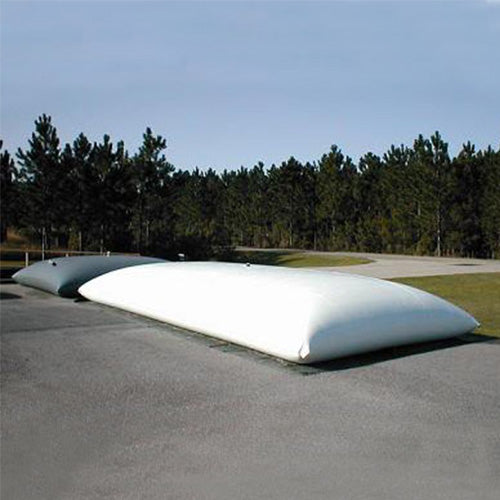 Large white inflatable water storage bladder placed on a paved surface outdoors, with a smaller gray bladder nearby, surrounded by trees and grass, ideal for emergency water storage or large-scale water management.