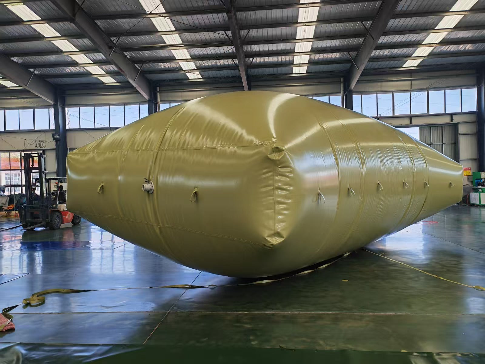 Large olive-green industrial inflatable storage bladder in a spacious warehouse with a forklift in the background.