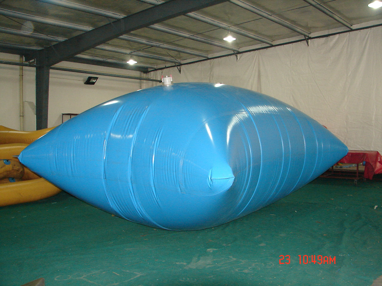 A Large blue inflatable water storage bladder with a white valve, placed indoors on a green surface, suitable for emergency water storage, industrial use, or large-scale water management.