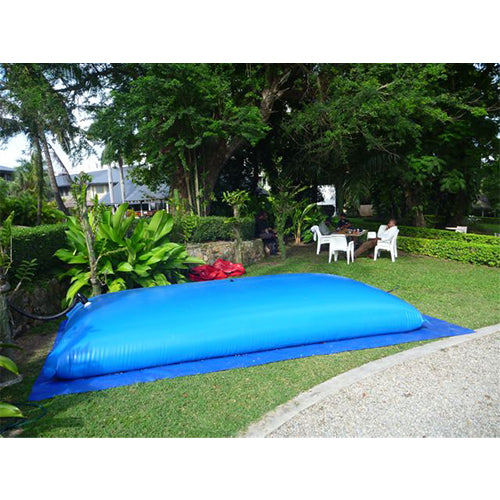 A large blue water storage bladder on a green lawn, surrounded by trees, plants, and outdoor furniture.