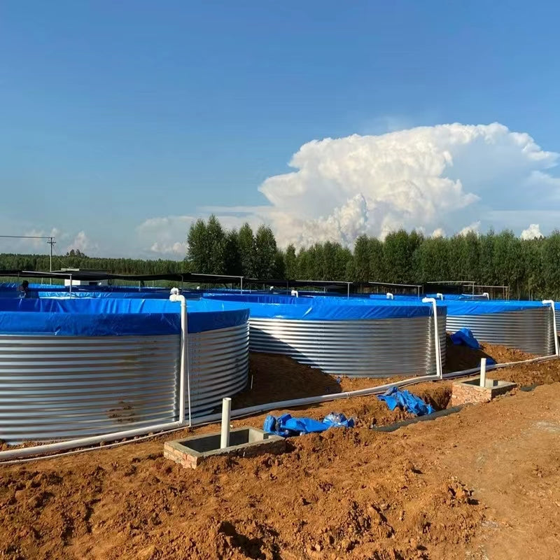 Three large blue-lined metal water tanks outdoors on a dirt surface, with pipes and construction materials nearby, ideal for agricultural or industrial water storage under a cloudy sky.
