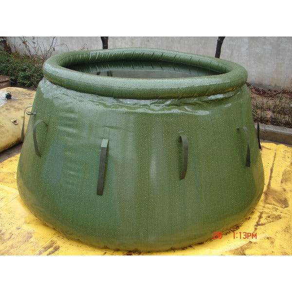 A large, green, circular collapsible water tank sits on a yellow tarp outdoors. The tank is made of a flexible material and has a thick, inflatable ring around the top.