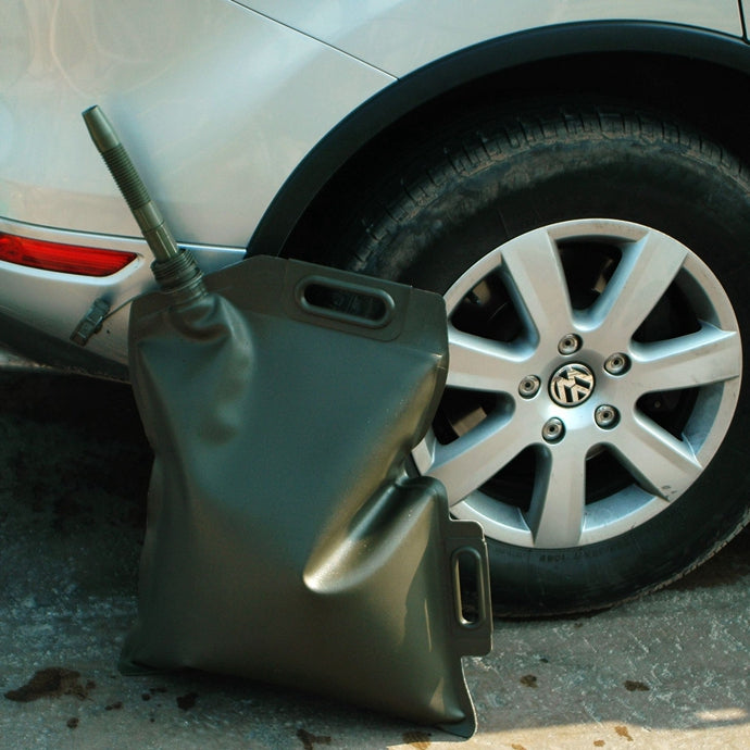 Green foldable fuel tank with a portable nozzle leaning against the tire of a silver Volkswagen vehicle.