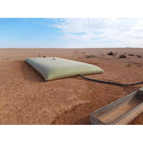 A rectangular, low-profile, light-colored flexible water storage tank (bladder) sits on dry, reddish-brown ground in a vast, arid landscape.